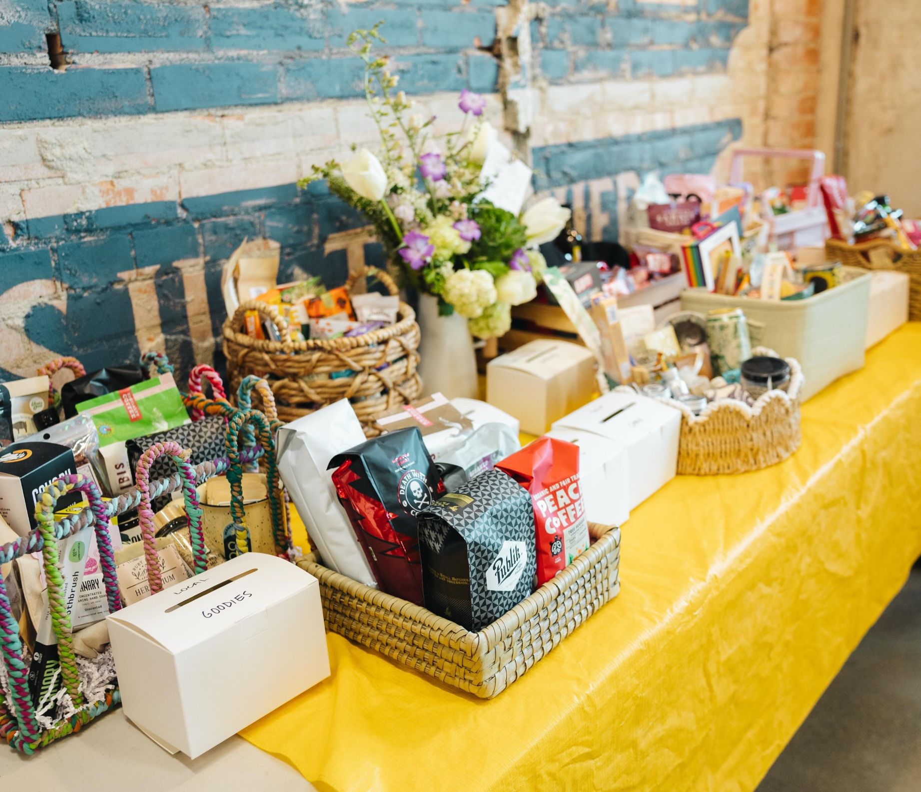 Various items like coffee flowers and snacks on a long table with a yellow table cloth at the Wasatch Food Co-op Grand Opening